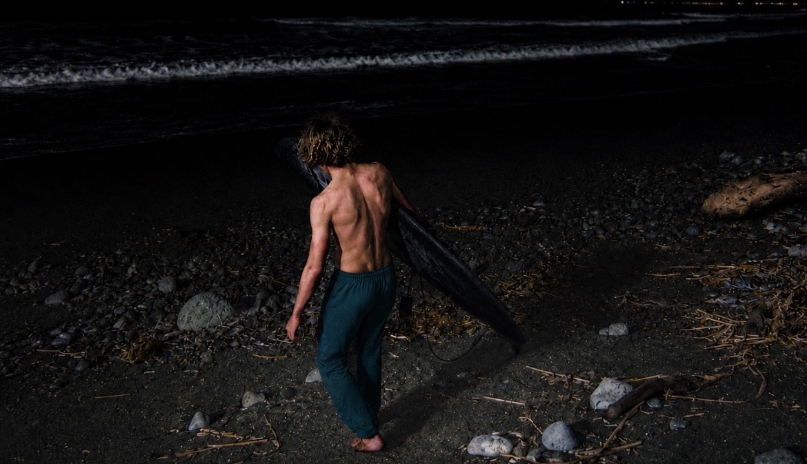Walking down the beach at night with a surfboard